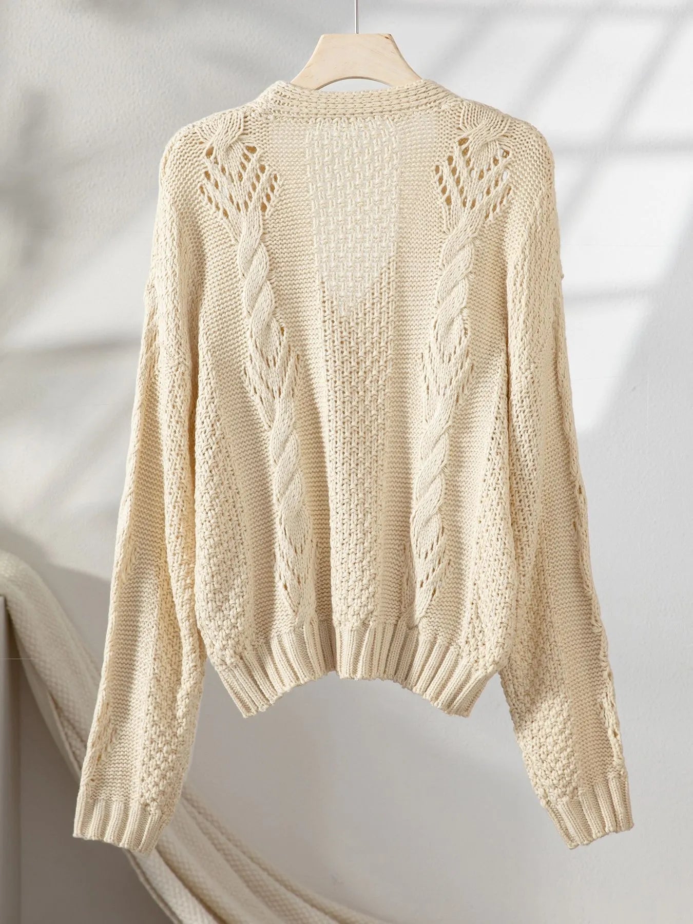 Beige cropped sweater cardigan with cable knit texture and long sleeves, back view