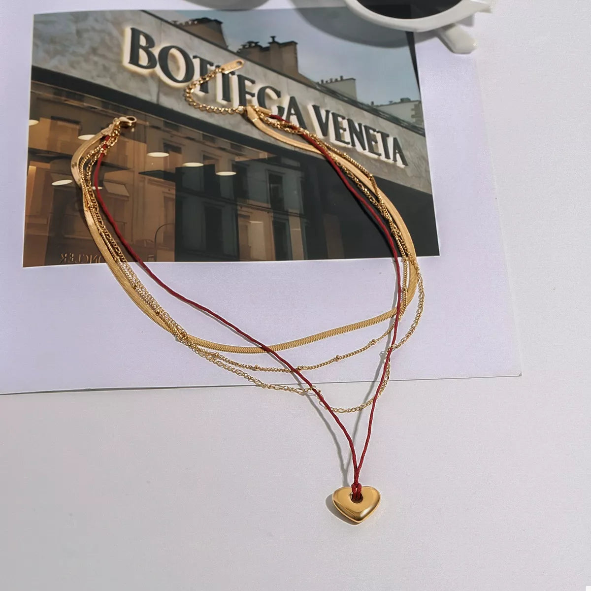 Gold four-layer heart necklace with red cord and heart pendant, flat lay on card.