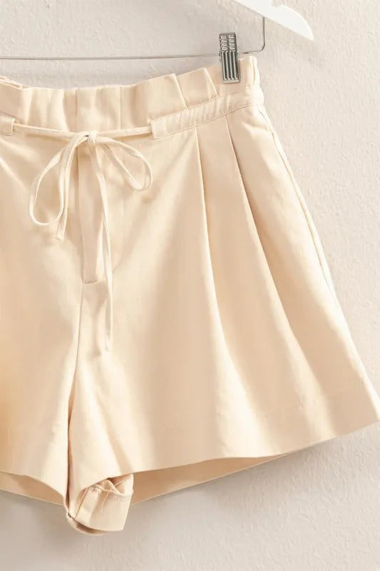 Oatmeal paperbag shorts close-up: elastic waistband, drawstring tie, pleated front