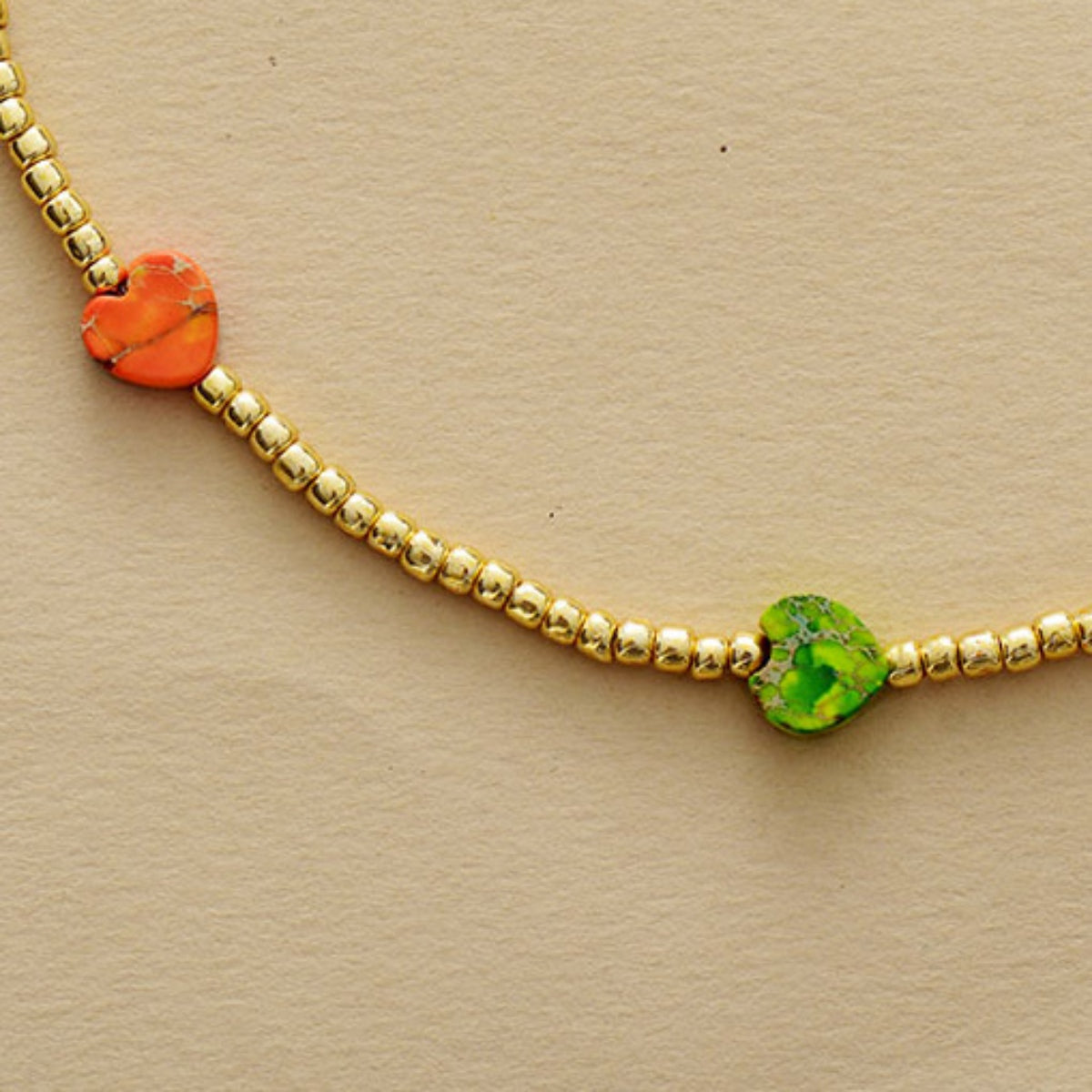 Gold-tone beaded necklace detail with orange heart stone and green center heart