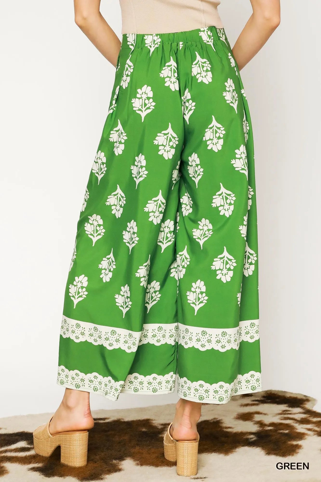 Green wide-leg pleated pants with white floral print and lace border at hem