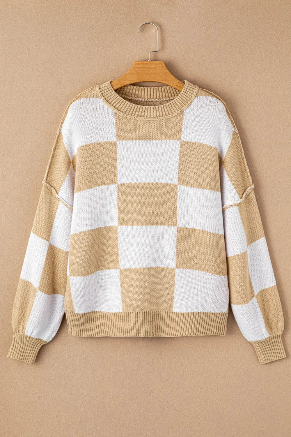 Tan and white checkered knit sweater on a hanger with ribbed crew neck and hem