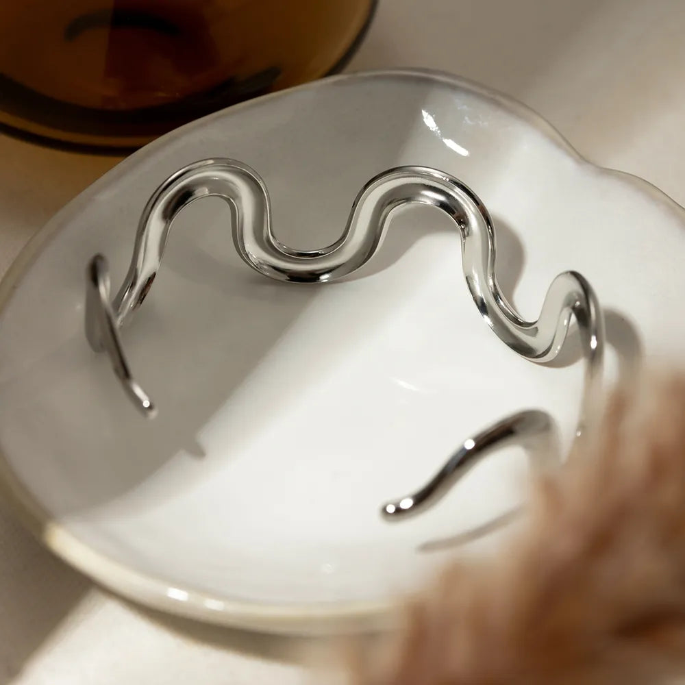 Wave-shaped stainless steel bracelet close-up, smooth wavy links and open ends.