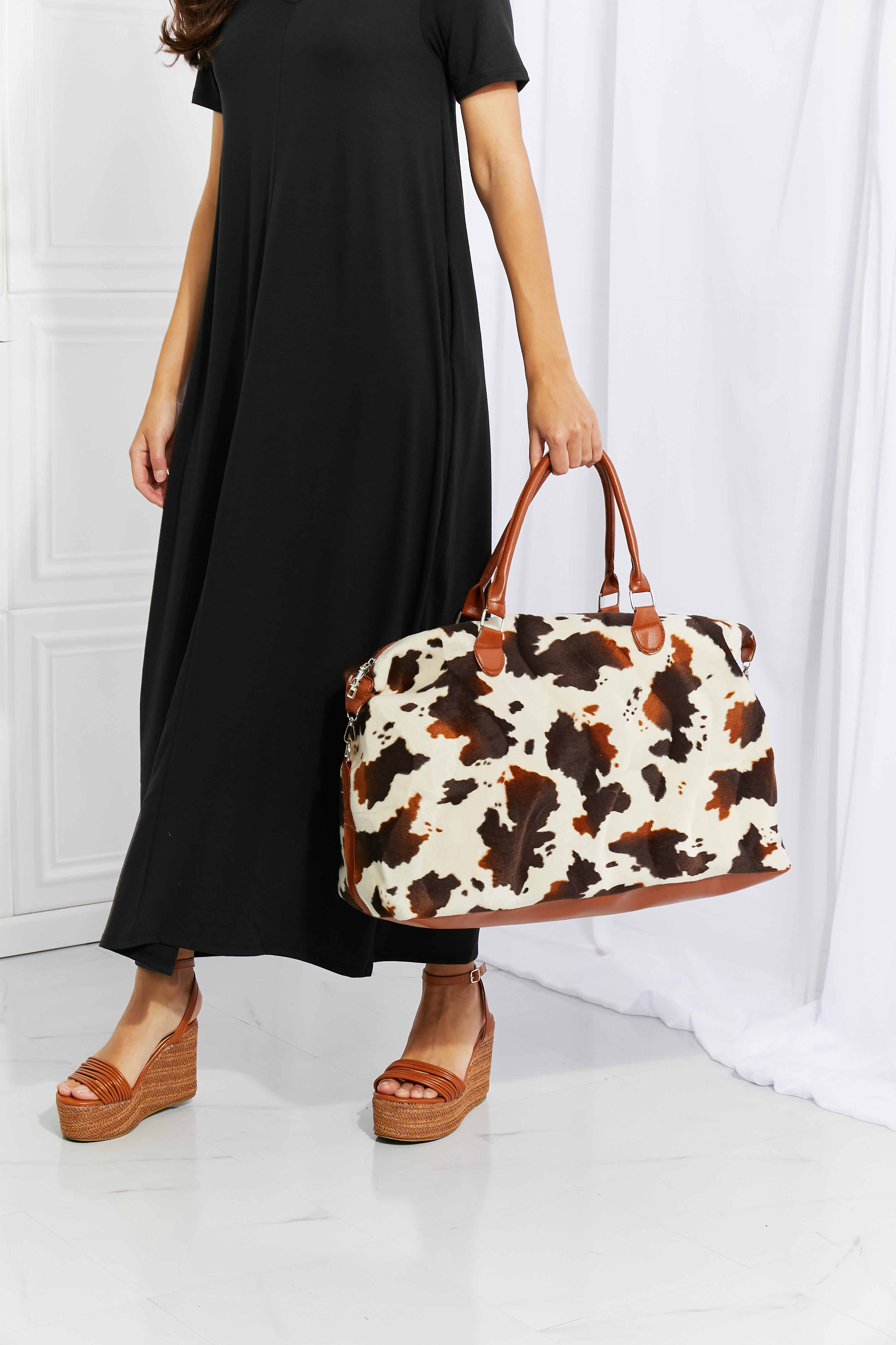 Animal print plush weekender bag, cow-spotted front with brown handles and rounded base