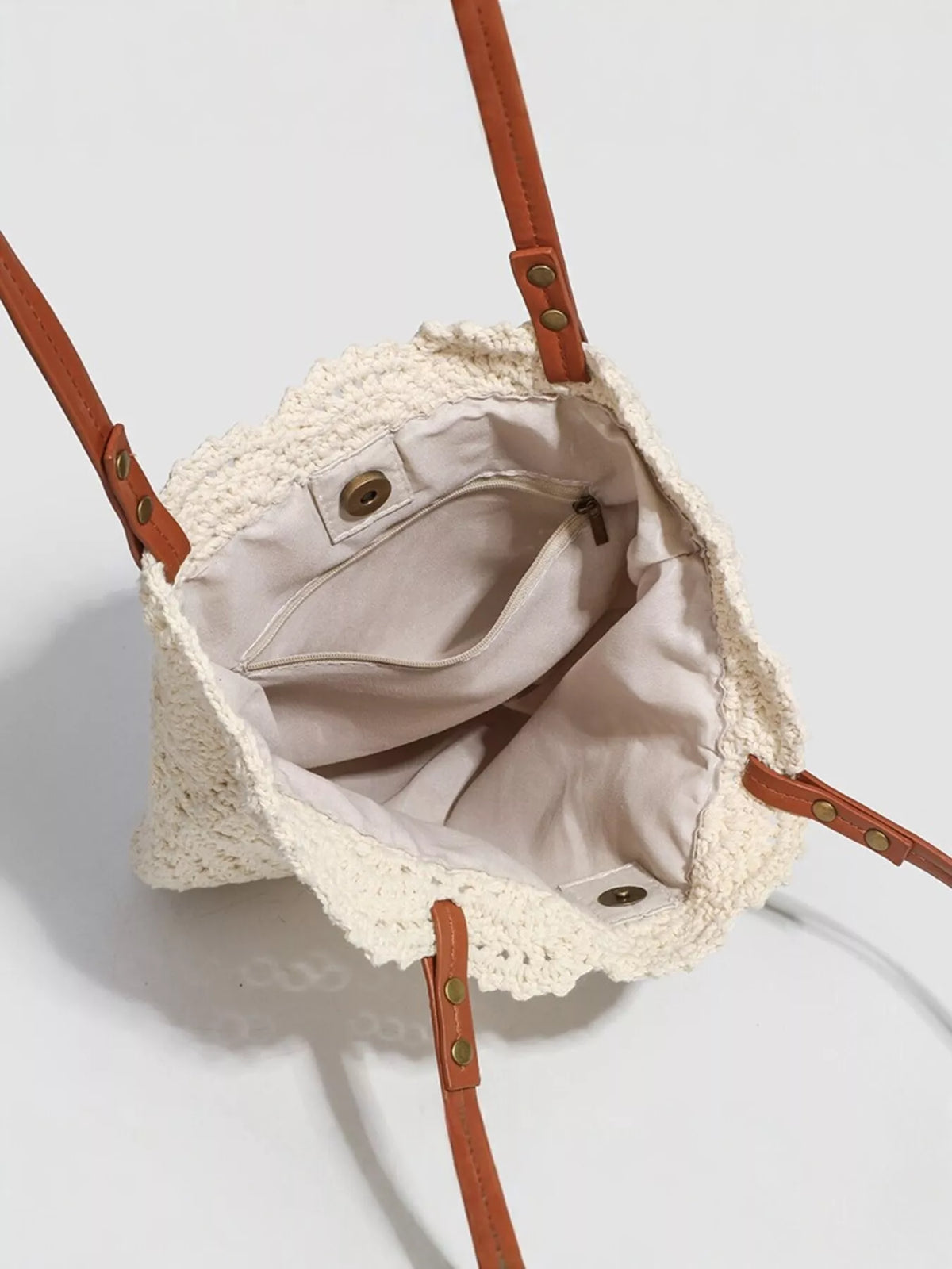 Crochet tote interior with beige lining, snap buttons, and brown leather trim.
