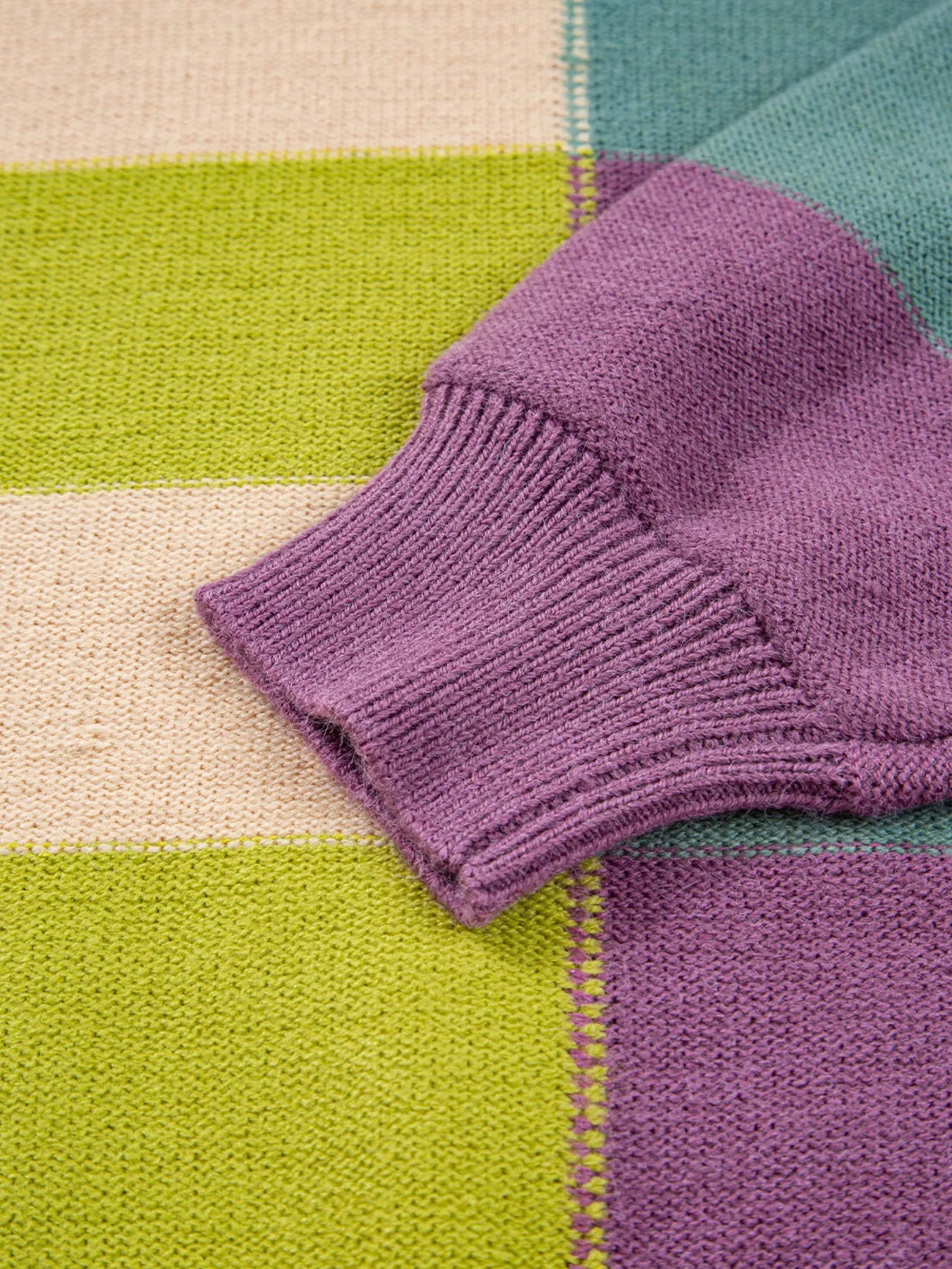 Purple ribbed knit cuff on multicolor striped sweater with green and cream blocks