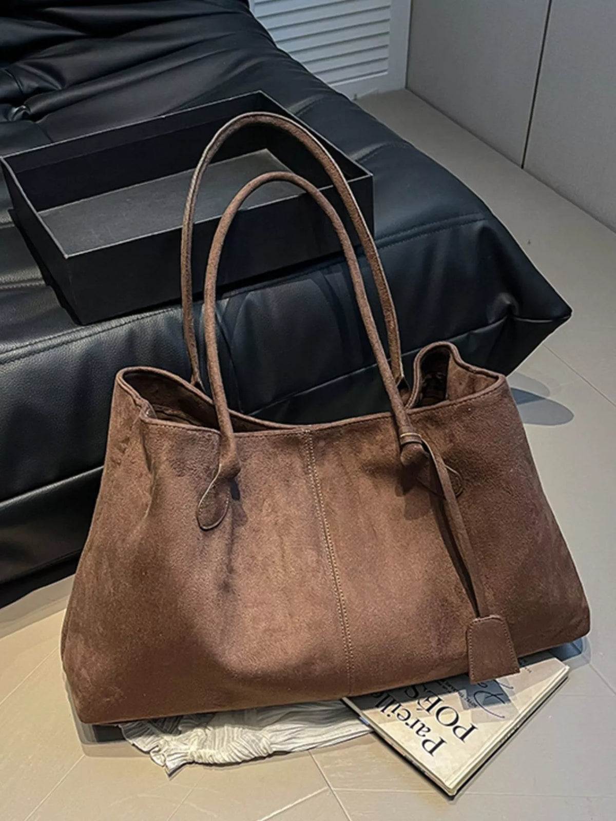 Brown suede tote bag on couch with dual handles and front flap with strap