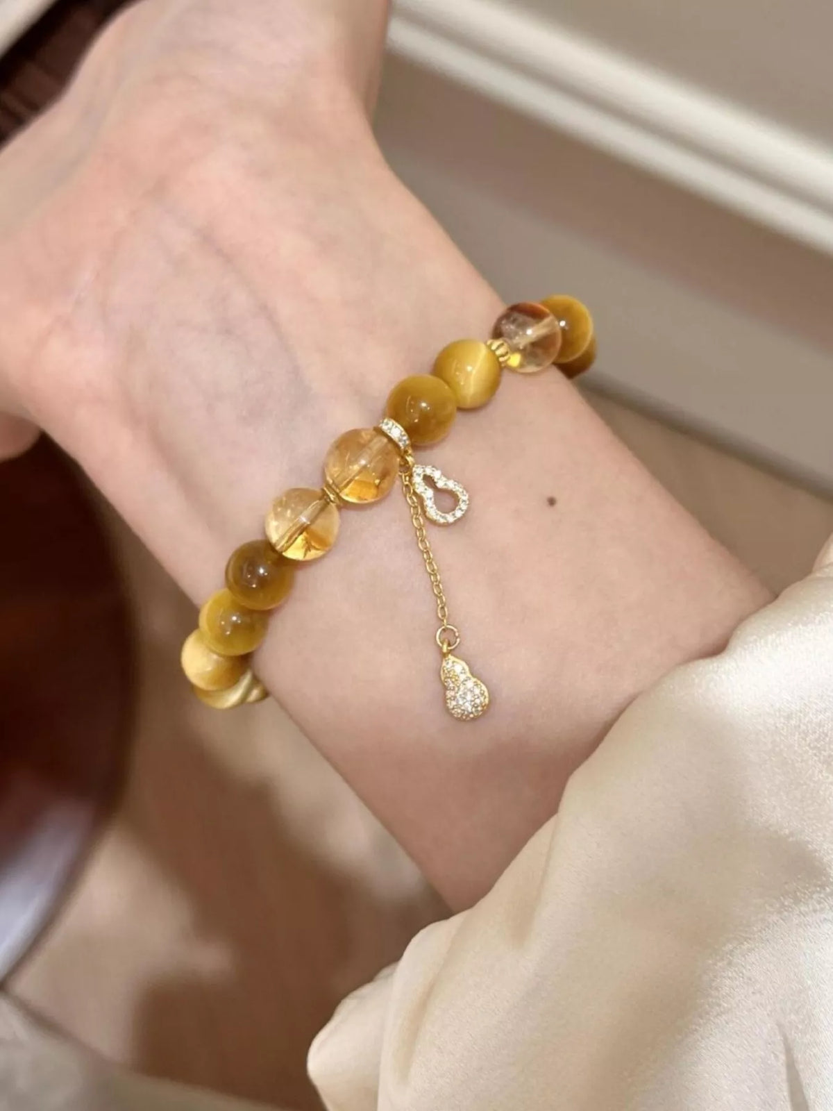Beaded bracelet wrist view, amber beads with gourd charm and metal loop
