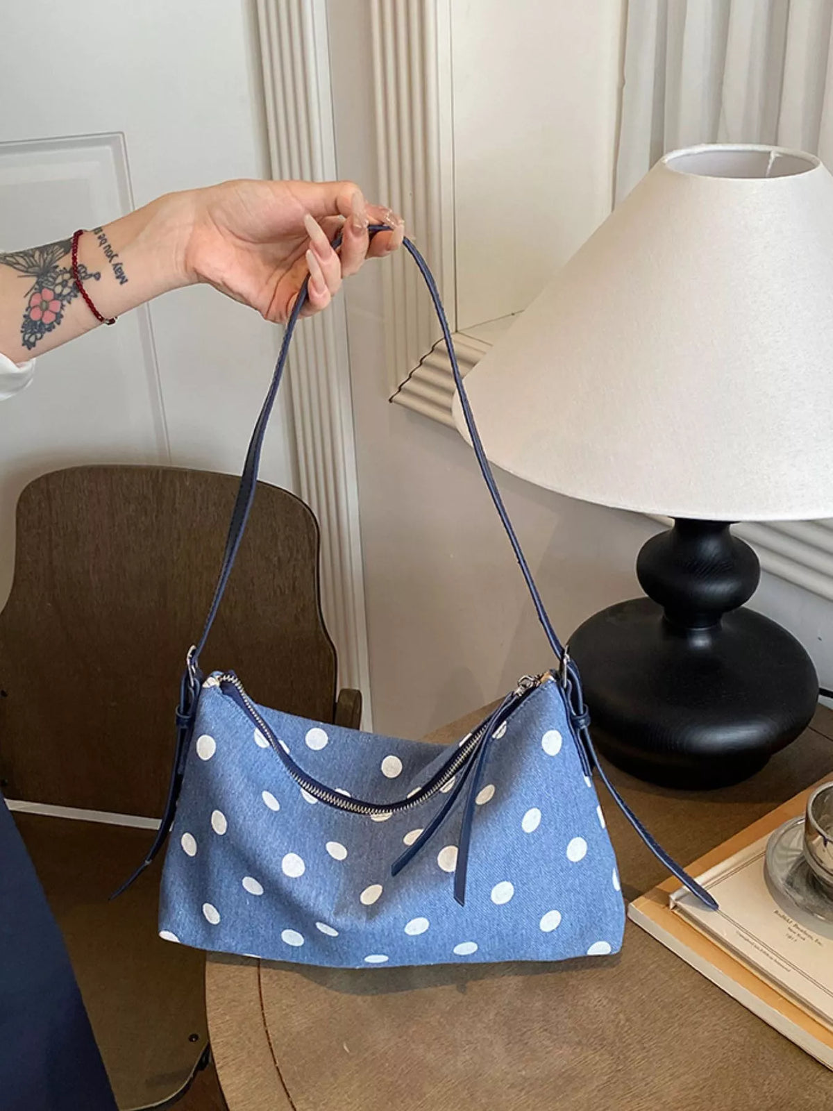 Blue polka dot tote-style shoulder bag with zipper top, held by long strap