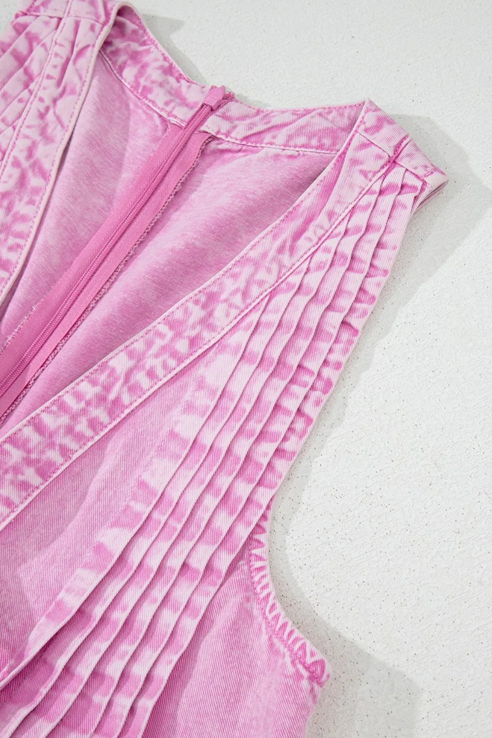 Pink mineral-wash denim romper close-up of pleated front panel and stitched seams