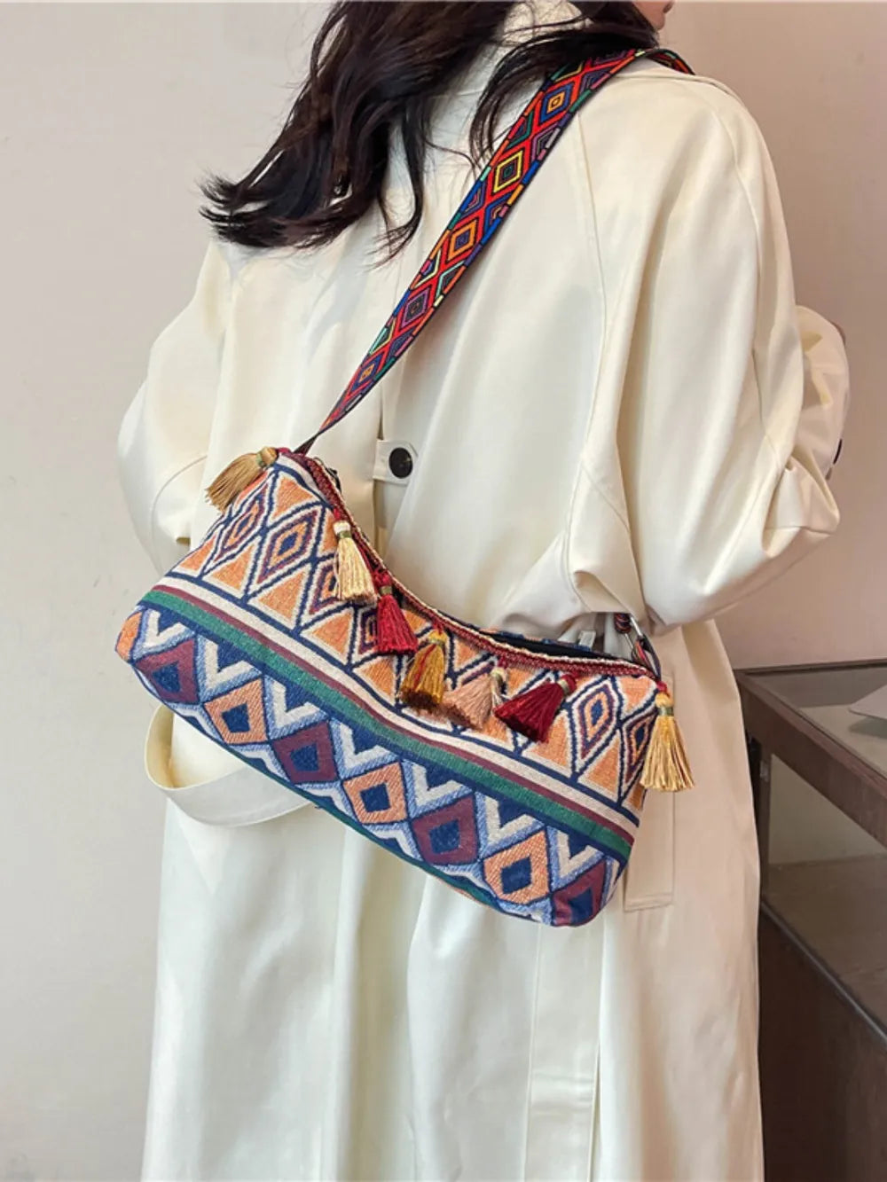 Geometric shoulder bag with adjustable strap and tassel trim, worn over a white dress