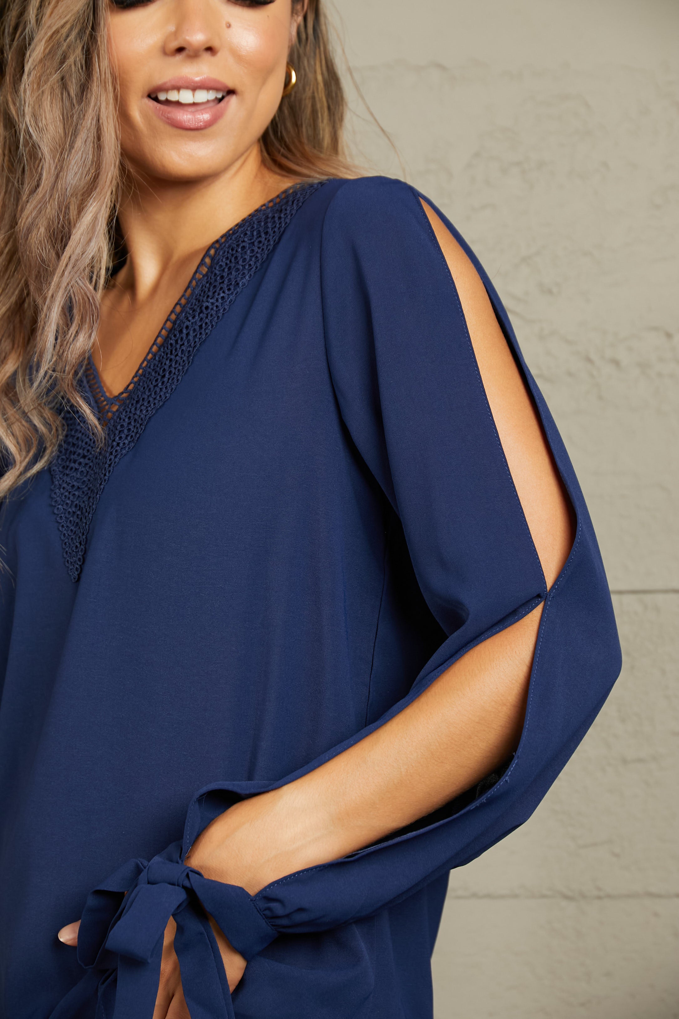 Dark blue V-neck blouse with crochet neckline and draped long sleeve with tie cuff