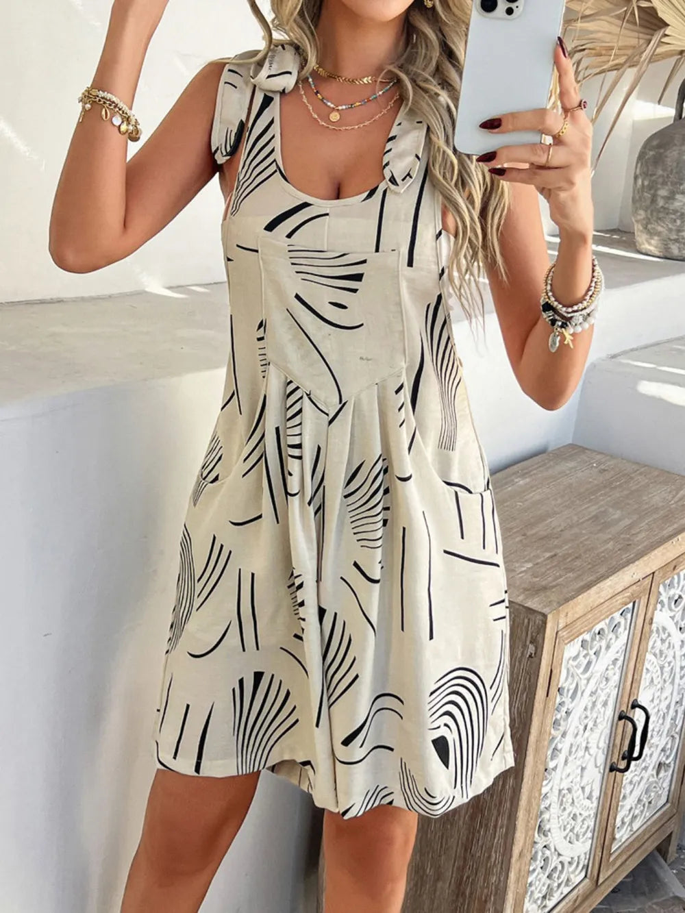 Printed tie-shoulder overall dress in light cream with black abstract pattern; front pocket panel