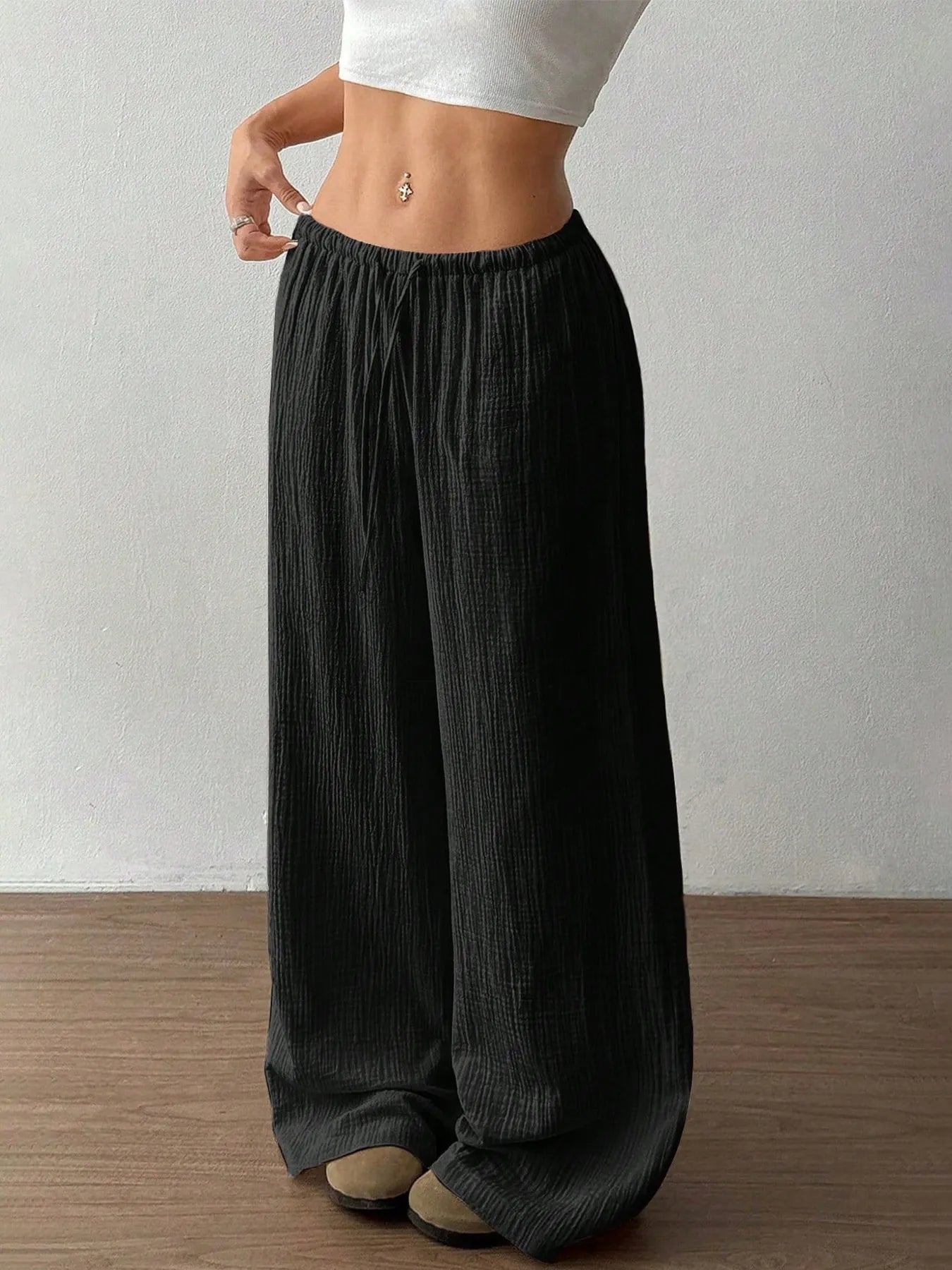 Black wide-leg pants with elastic waistband and drawstring, side profile.