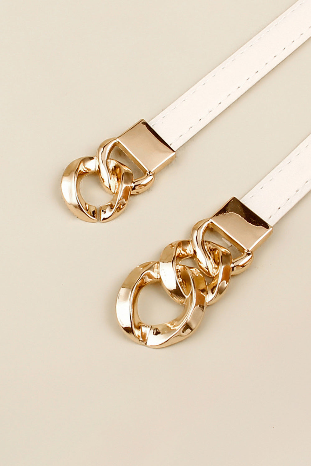 Gold chain-link buckle on a skinny vegan leather belt, white strap