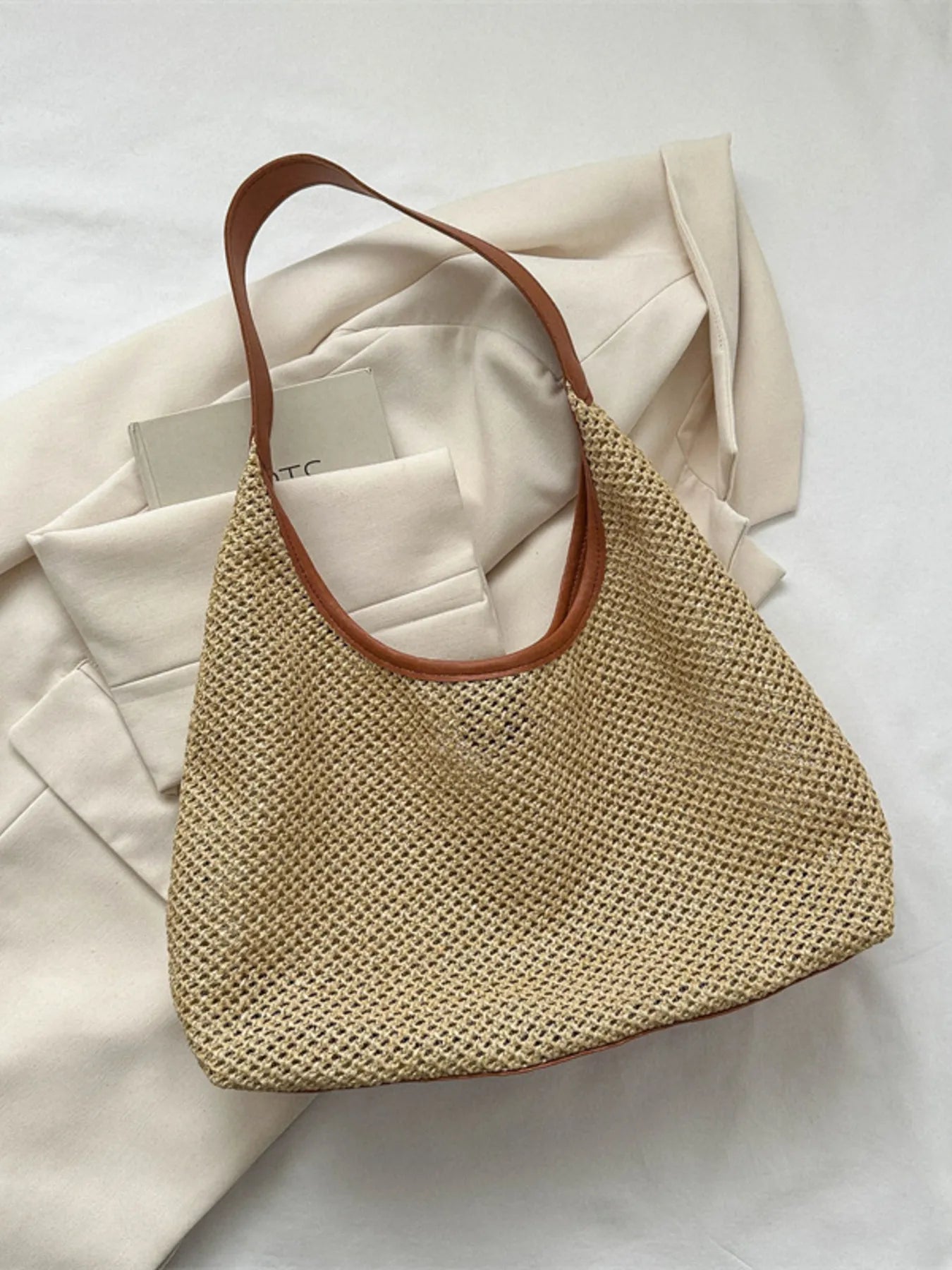 Woven straw shoulder bag in tan with brown leather handles, open-top hobo