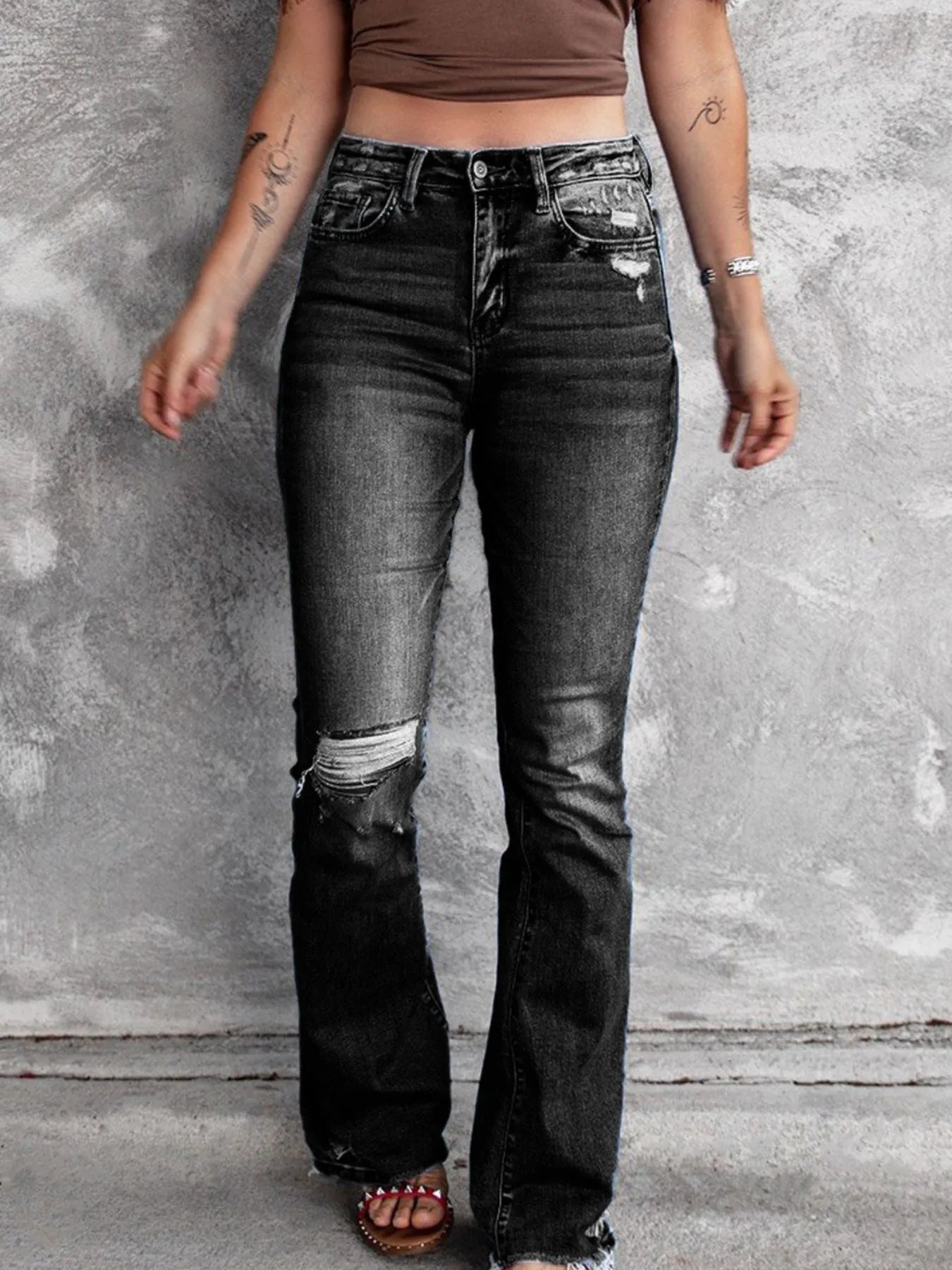 Black distressed flare jeans with ripped lower legs and faded panels on the thighs