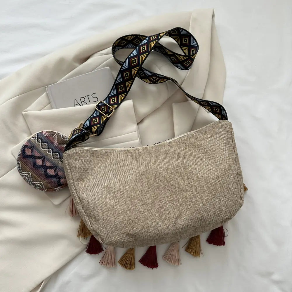 Linen-tone crossbody bag with patterned strap, tassel fringe, and coin pouch.