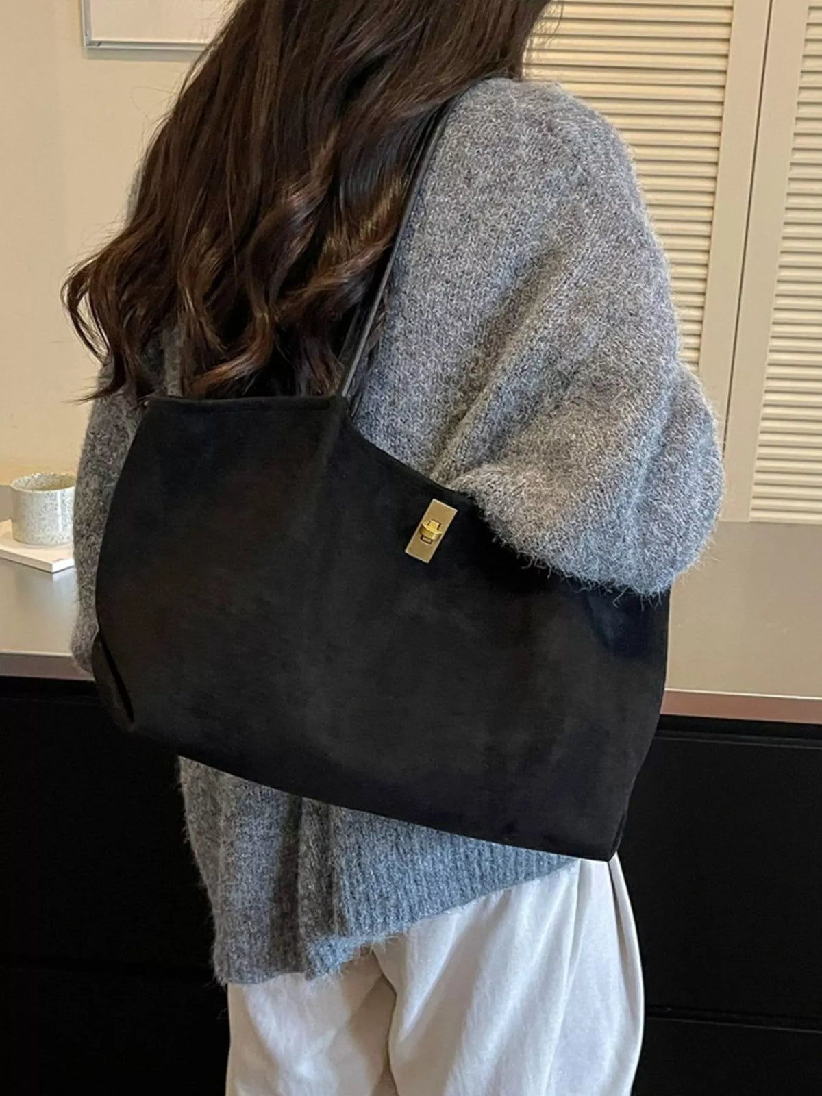 Black suede tote bag with gold turn-lock clasp and structured top handles