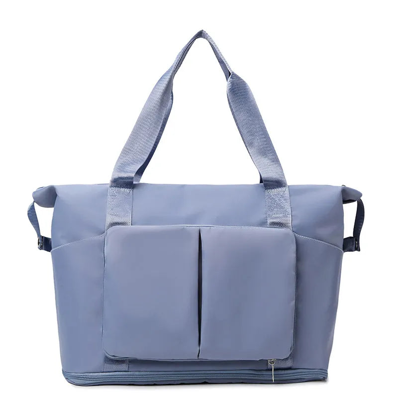 Light blue travel duffel bag with front organizer pocket, top handles, and side carry straps.