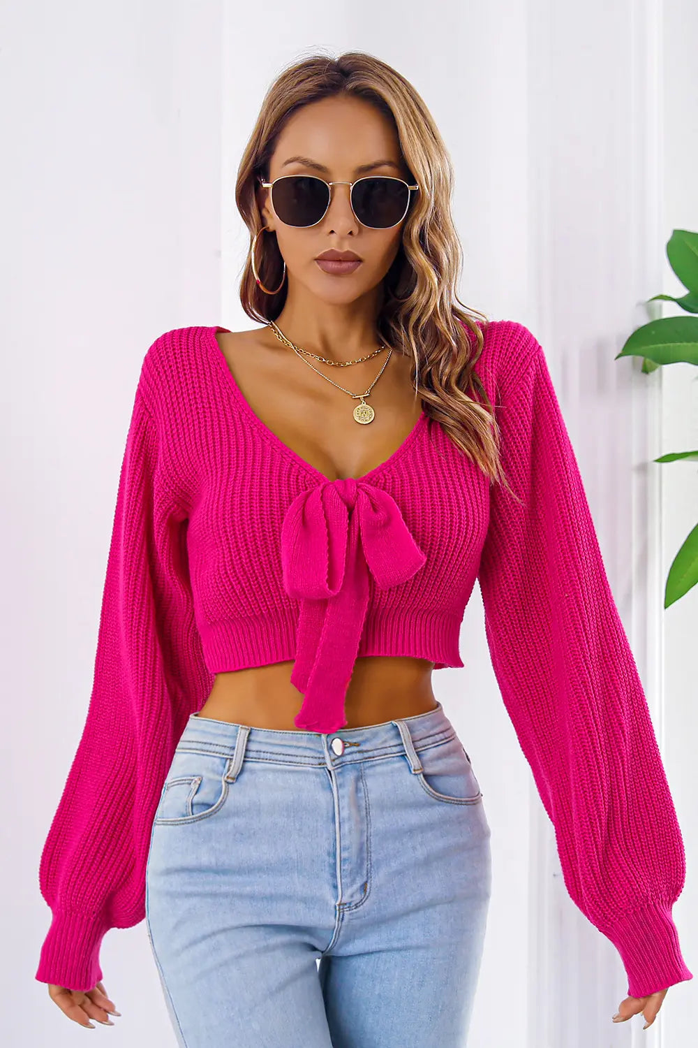 Deep rose knit cropped sweater with long sleeves, V-neck and tied bow at chest.