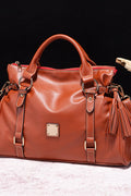 PU leather handbag in brown with tassel details, top handles, and front zipper pocket.