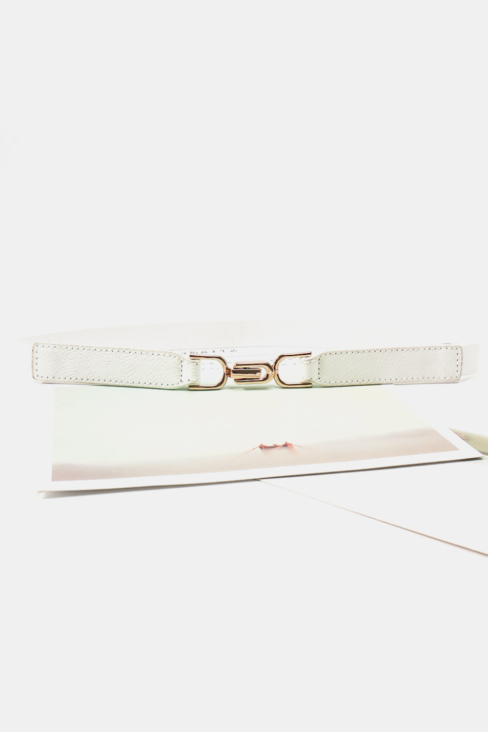 White elastic buckle belt laid flat with silver-tone center D-shaped hardware
