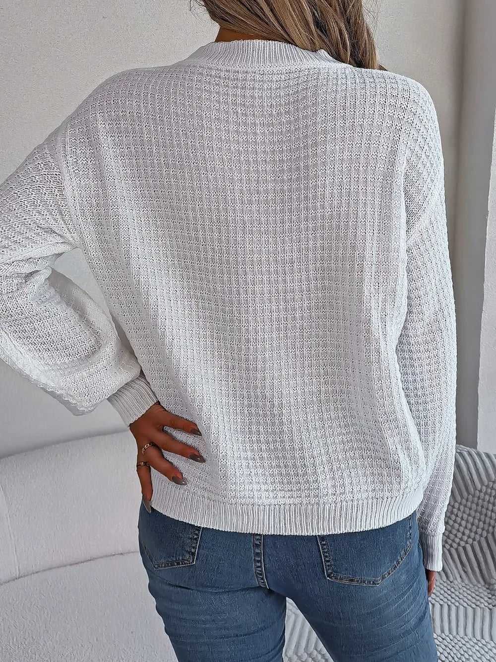 White cable-knit sweater back view with round neck, long sleeves, and ribbed hem.