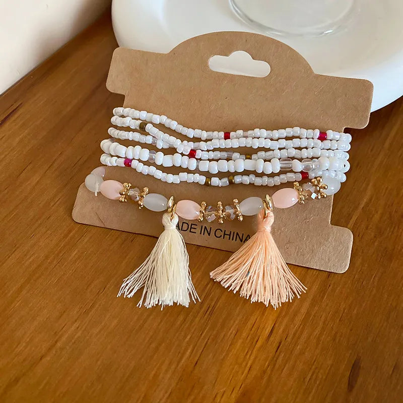White beaded tassel bracelet with pink bead accents and two beige tassels