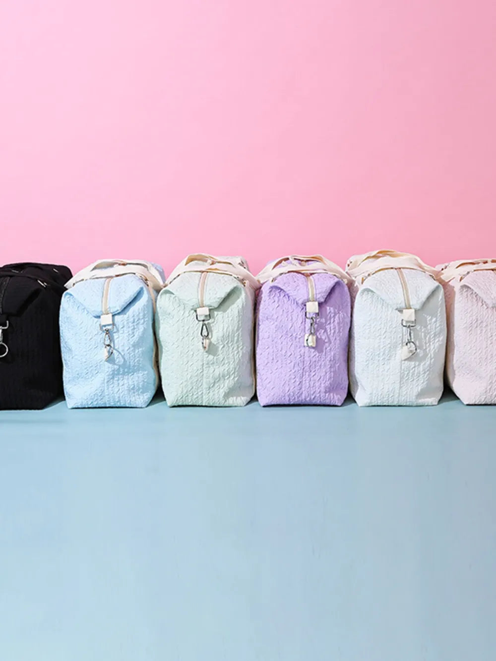Stacked large duffle travel bags in dark, blue, lavender, and light tones