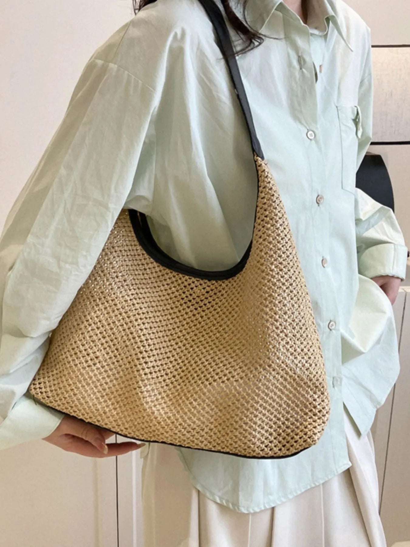 Woven straw shoulder bag in tan with black handles, open-top hobo style