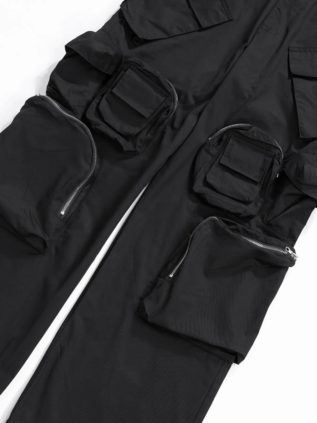 Black utility cargo pants thigh pockets with flap closures and zipper accents, close-up.