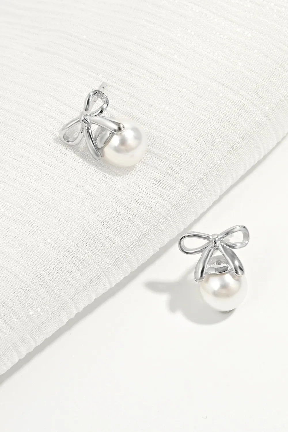 Silver bow stud earrings with pearl spheres beneath ribbon bow details.