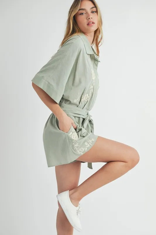 Dusty sage side view romper with collared button front, waist tie, and embroidery