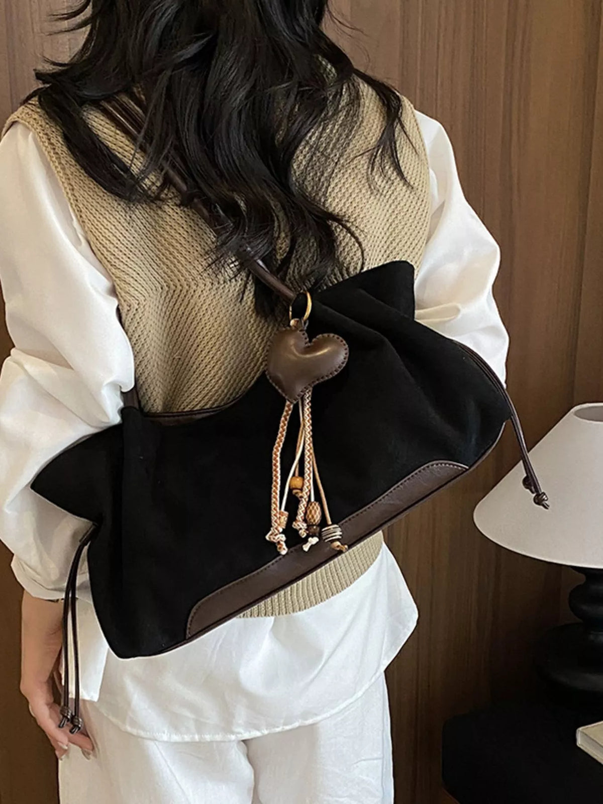 Black suede drawstring shoulder bag close-up: heart charm, braided tassels, suede straps
