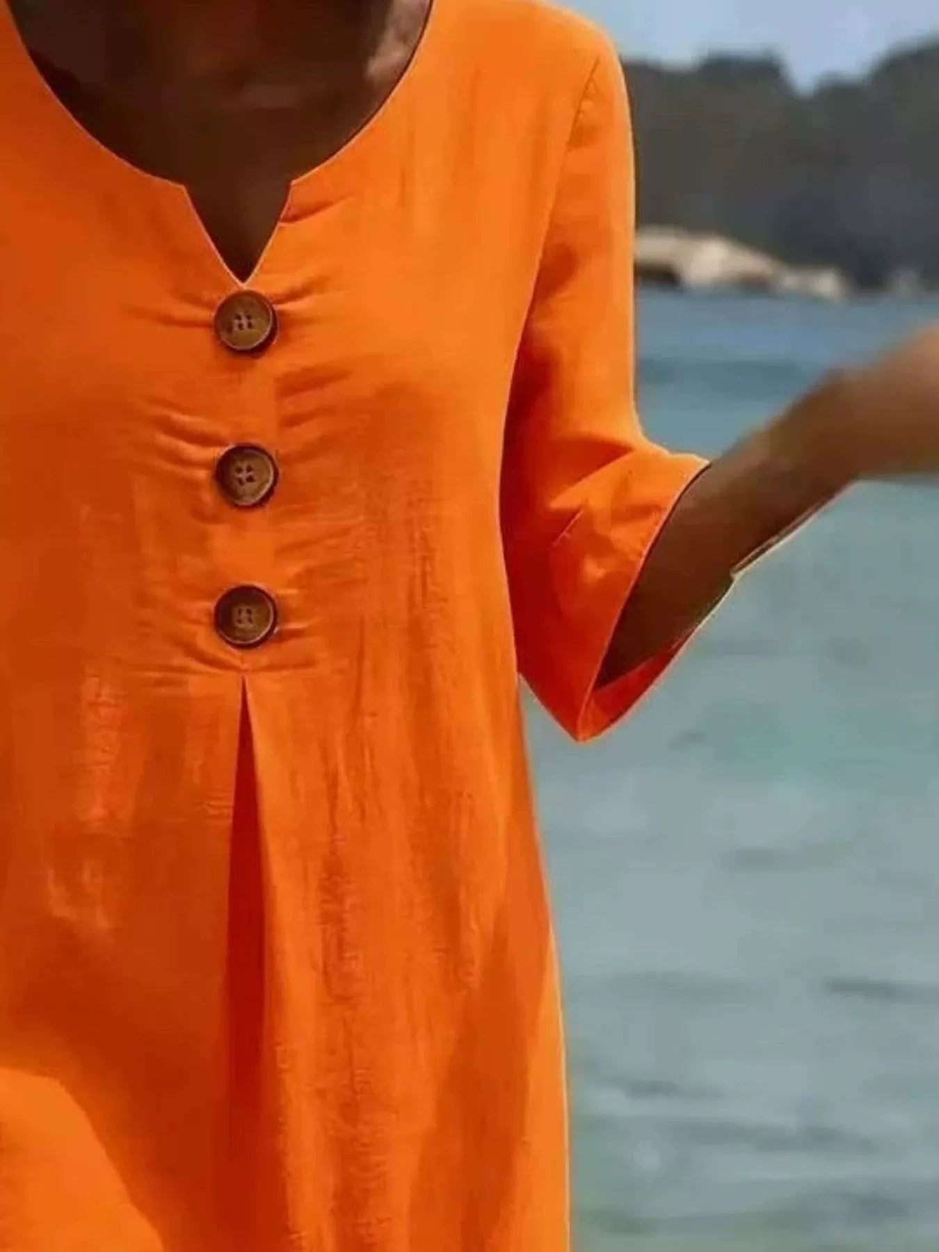 Orange button-front dress close-up with V-neck and three wood-look buttons, ruffle cuff