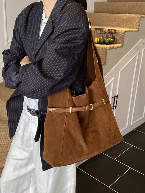 Brown suede bucket shoulder bag with adjustable strap and centered metal buckle detail.