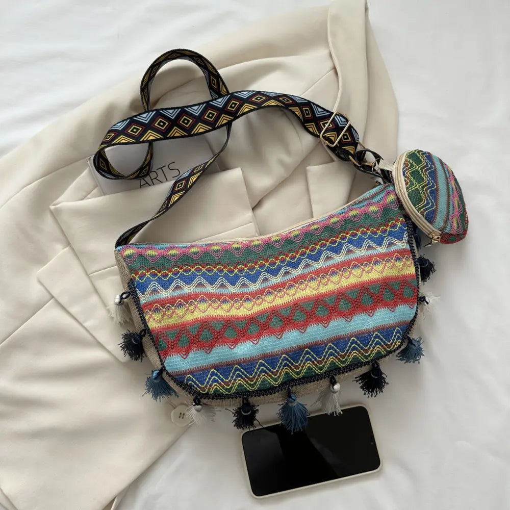 Printed crossbody bag with zigzag stripes, zipper top, tassels, and coin pouch.
