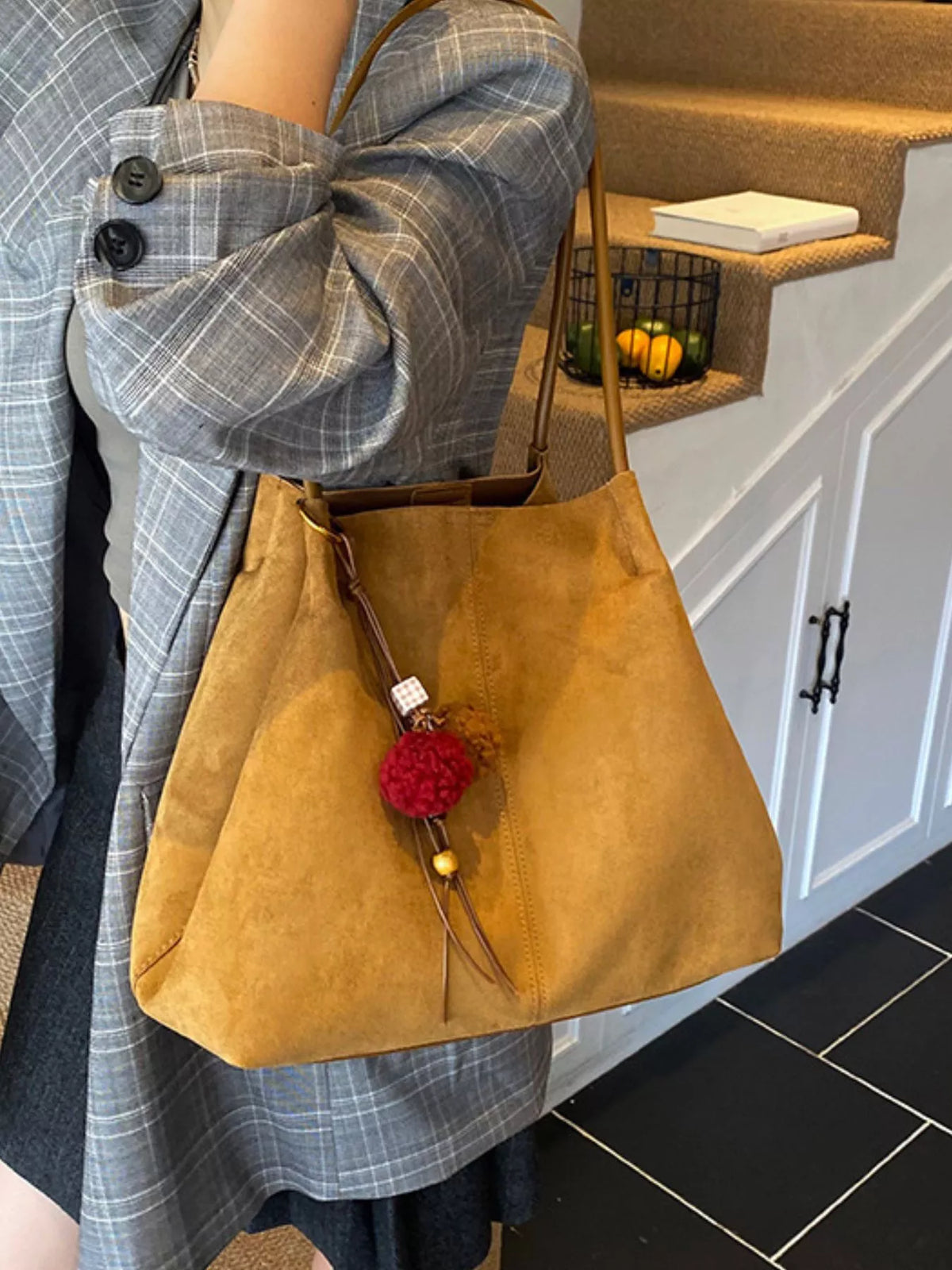 Tan suede tote bag with long handles, front zip pocket, and pom-pom charm.