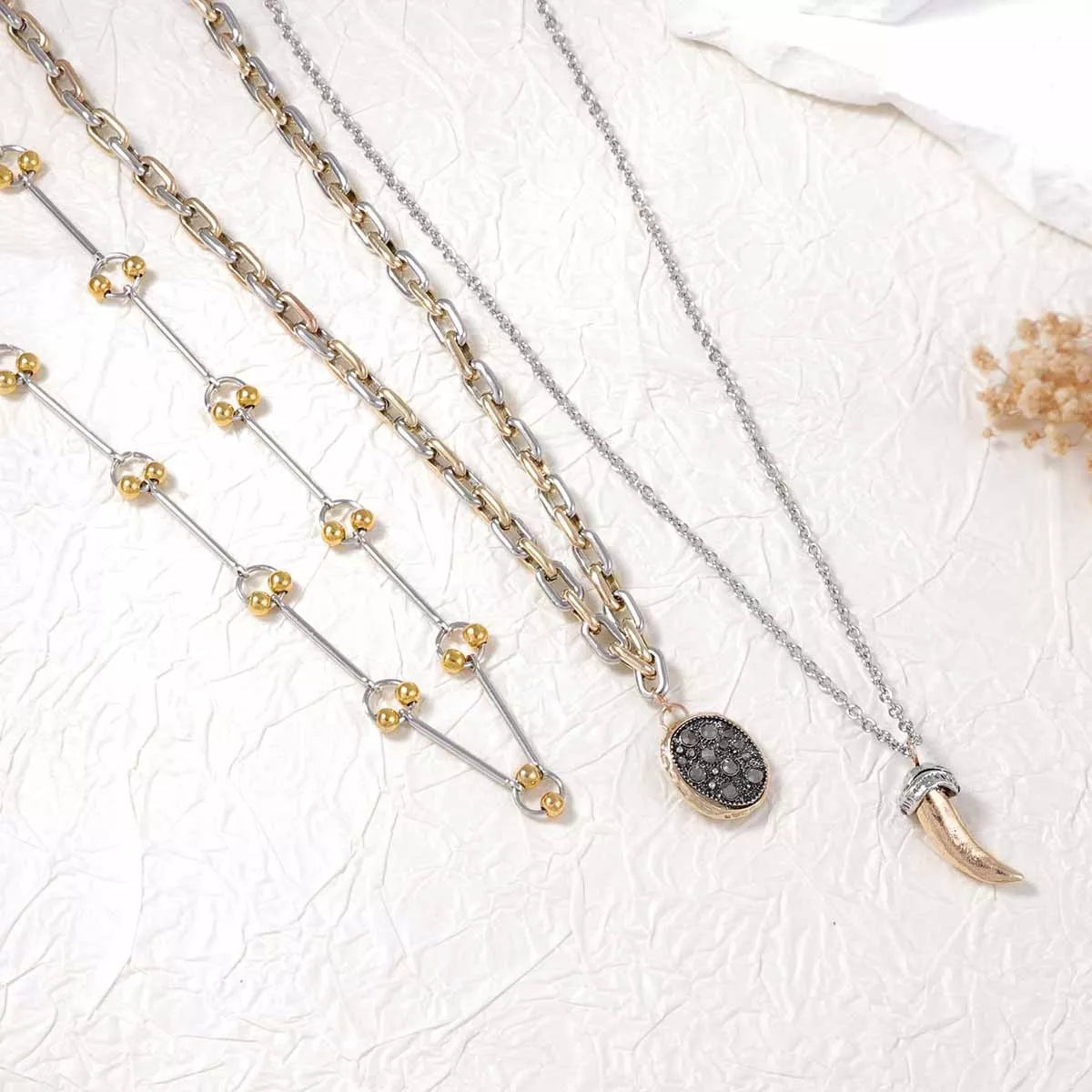 Close-up of layered gold and silver-toned chains with dark round pendant and horn charm