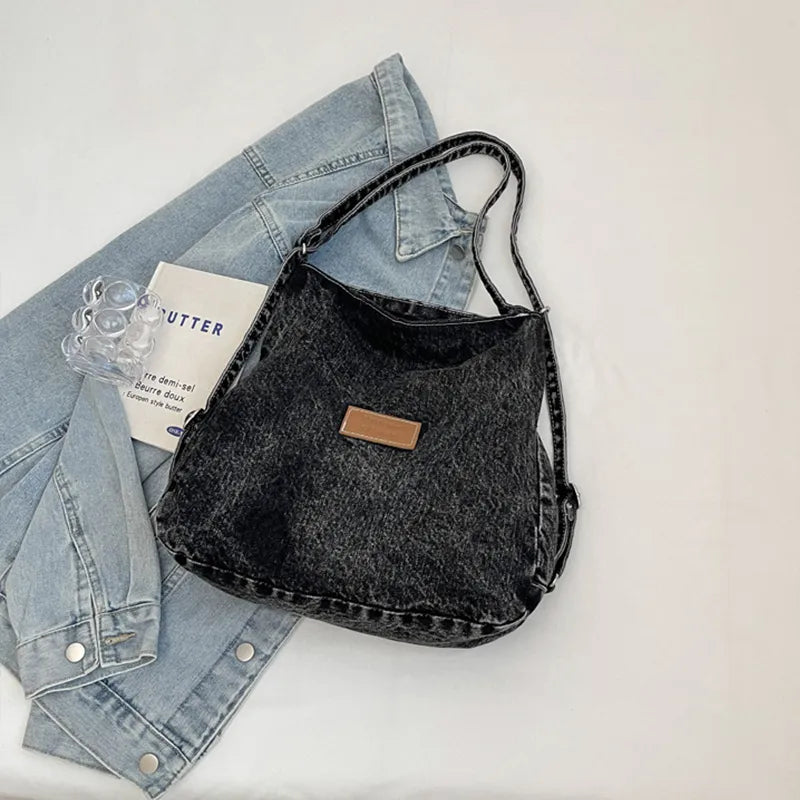 Black denim shoulder bag with adjustable strap and rectangular leather logo patch