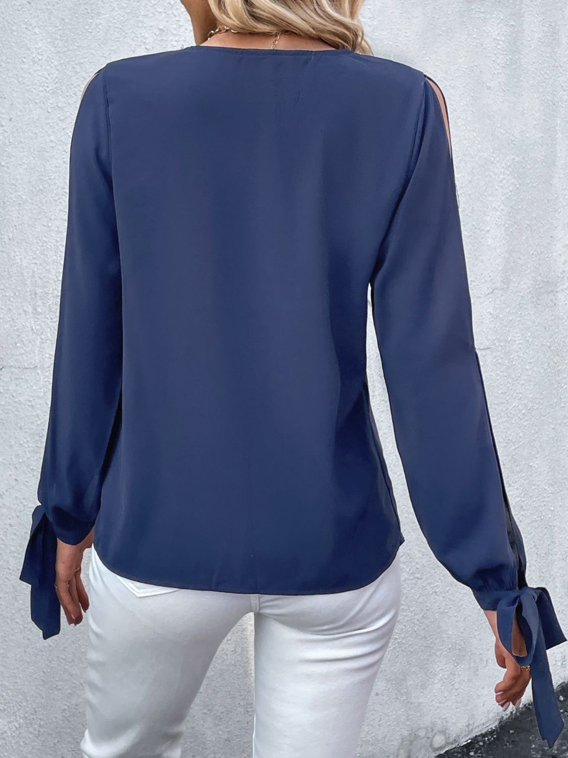 Back view of dark blue V-neck blouse with long sleeves and tie cuffs