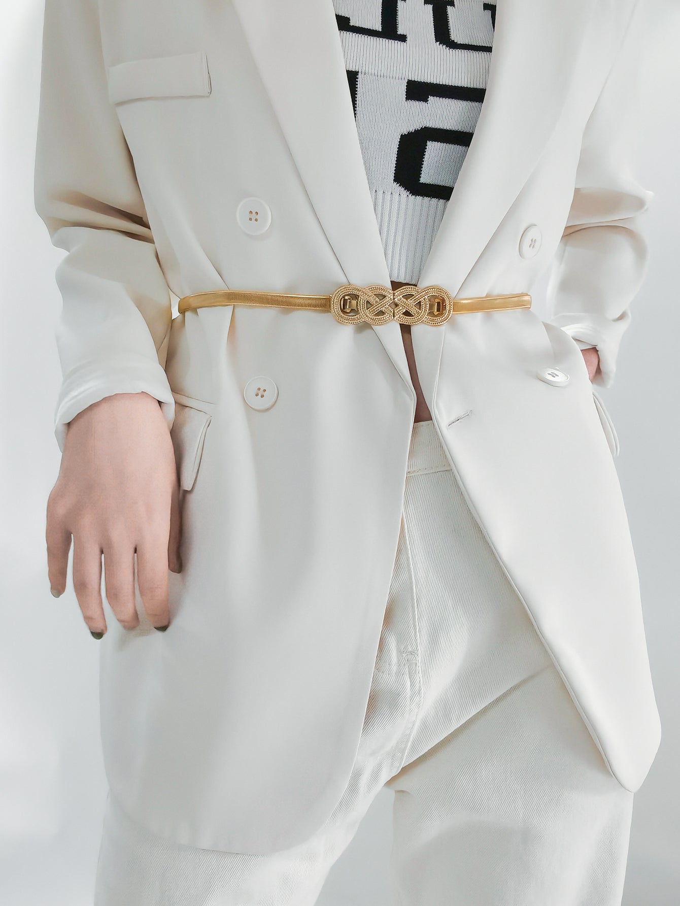 Gold-tone metal knot buckle belt with braided knot detail, worn on light pants