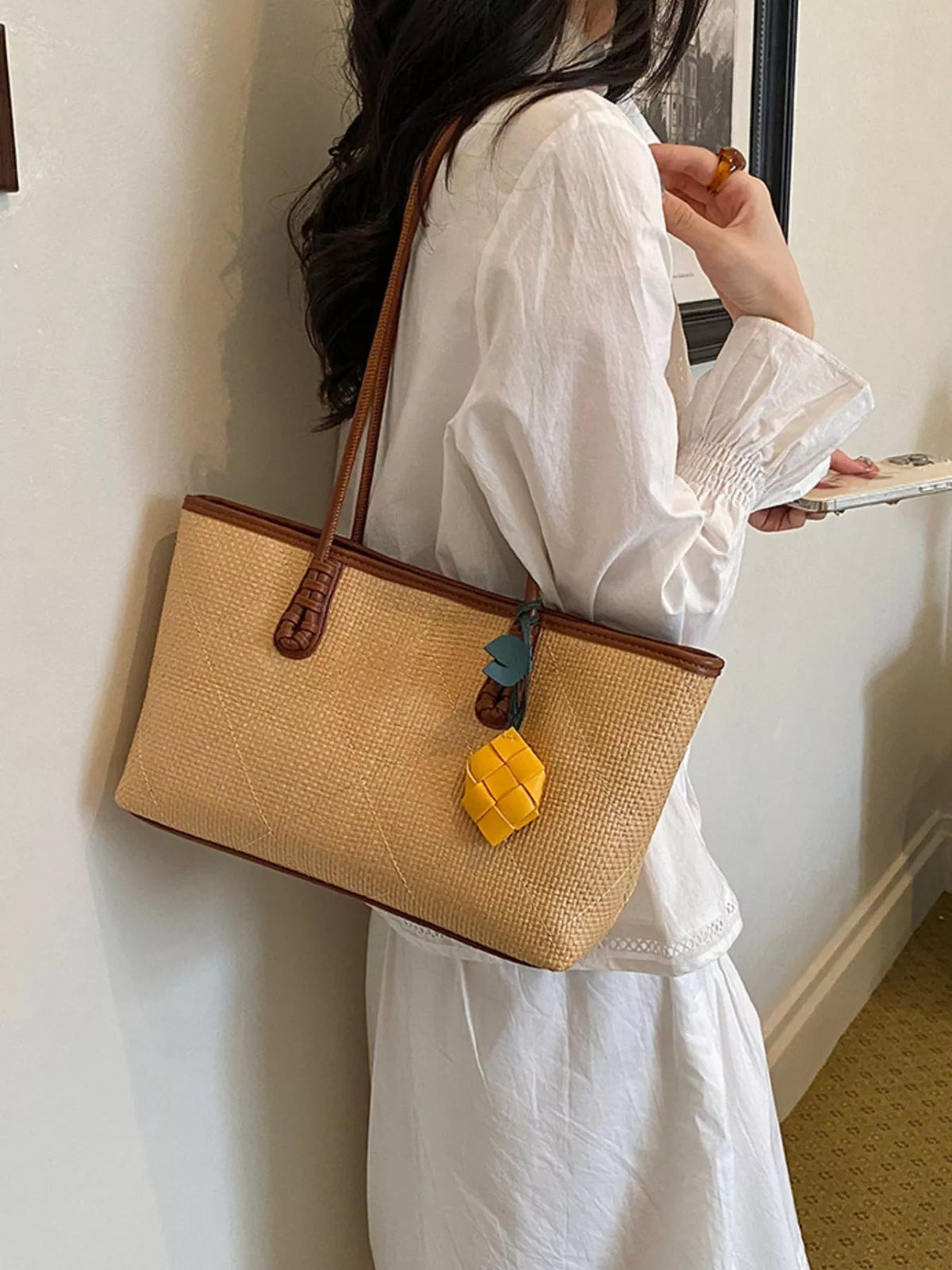 Beige leather shoulder bag with brown trim and yellow charm, side view