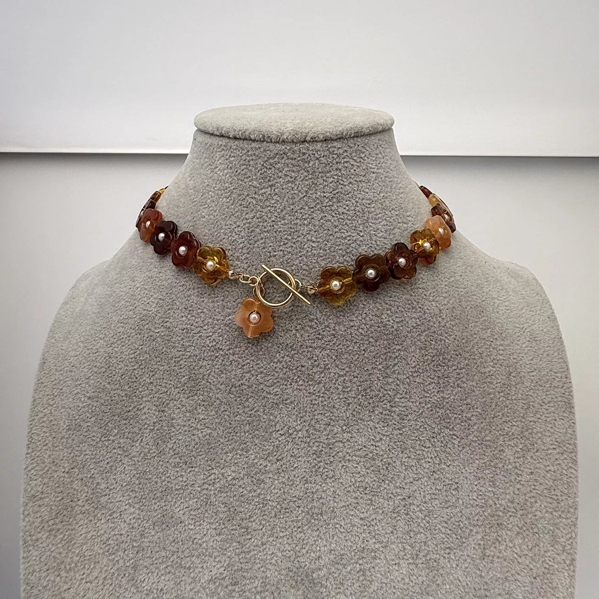 Gold beaded necklace on bust form with amber and dark brown resin flower charm drops