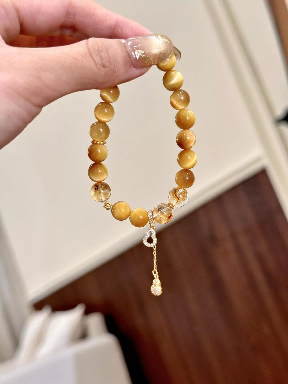 Beaded bracelet held up, round amber beads with gourd charm and clasp