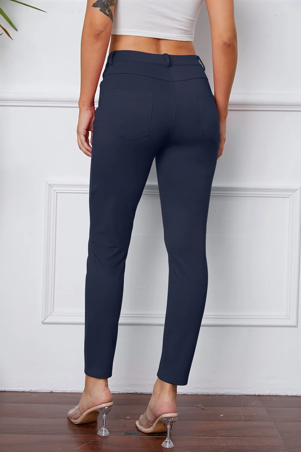 Stretchy dark blue pants, rear view, with button waistband and slim ankle-length leg