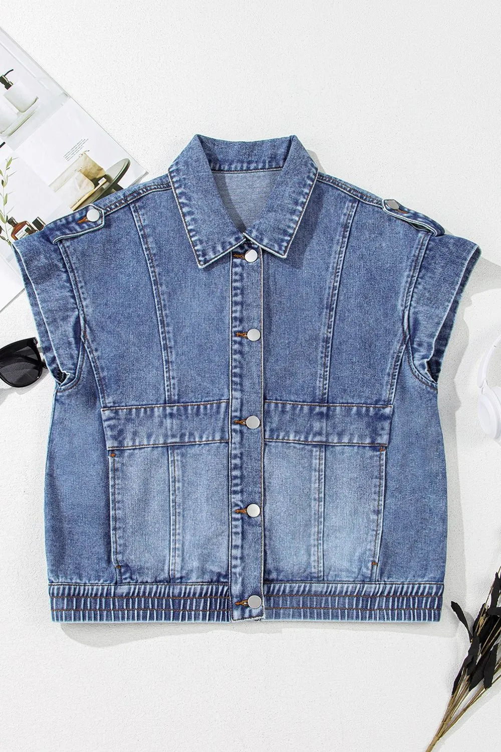 Medium-wash denim button-up cap sleeve jacket on flat lay, front view with patch pockets