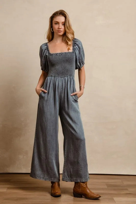 Washed denim jumpsuit with smocked square neckline, puff sleeves, wide-leg pants