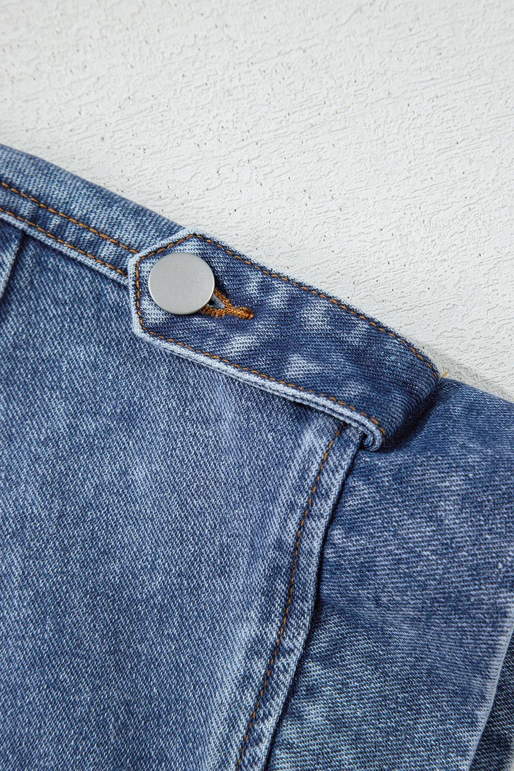 Denim jacket flap with round button detail and stitched edge